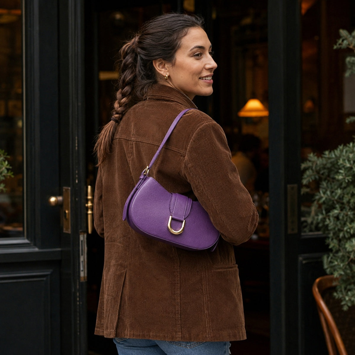 Sac baguette cuir violet a boucle doree porte a l epaule a l entree d un restaurant