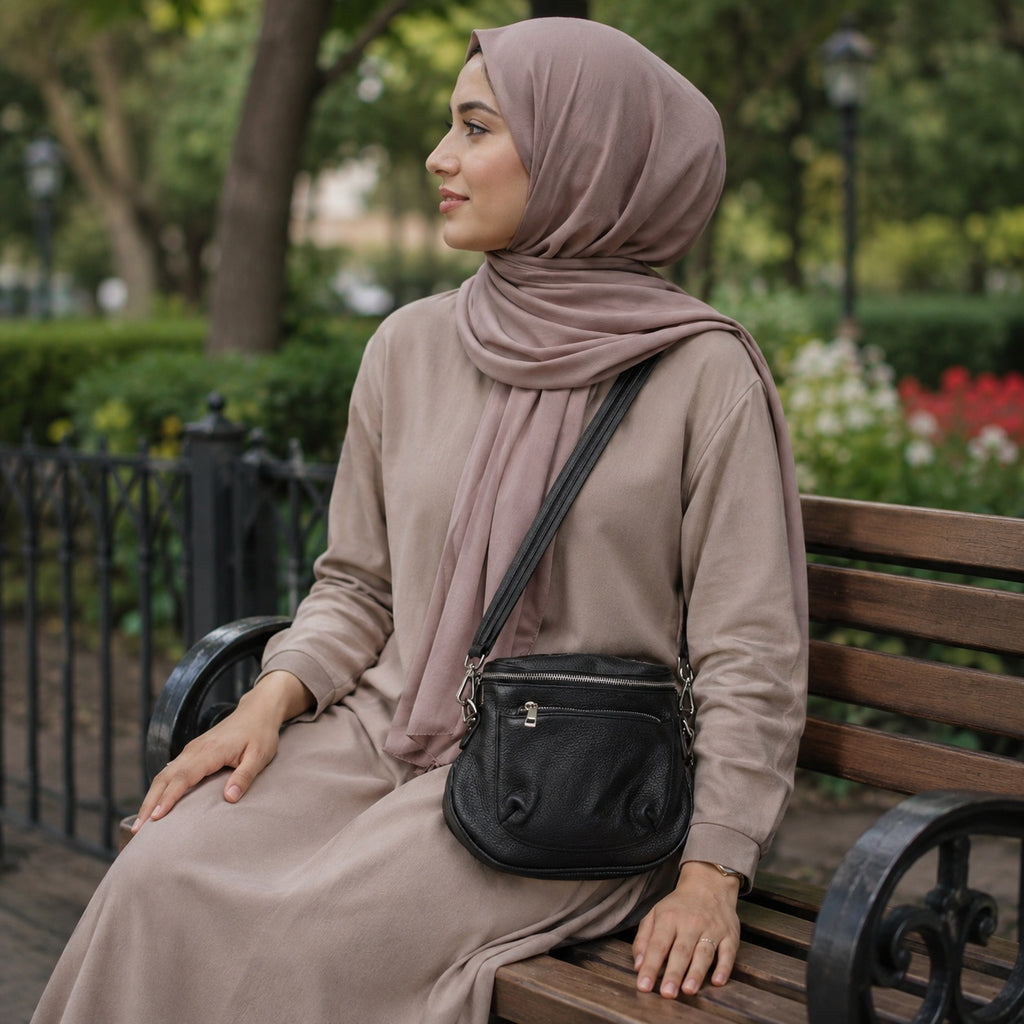 Sac bandouliere cuir noir zippe porte en croix sur un banc de jardin public